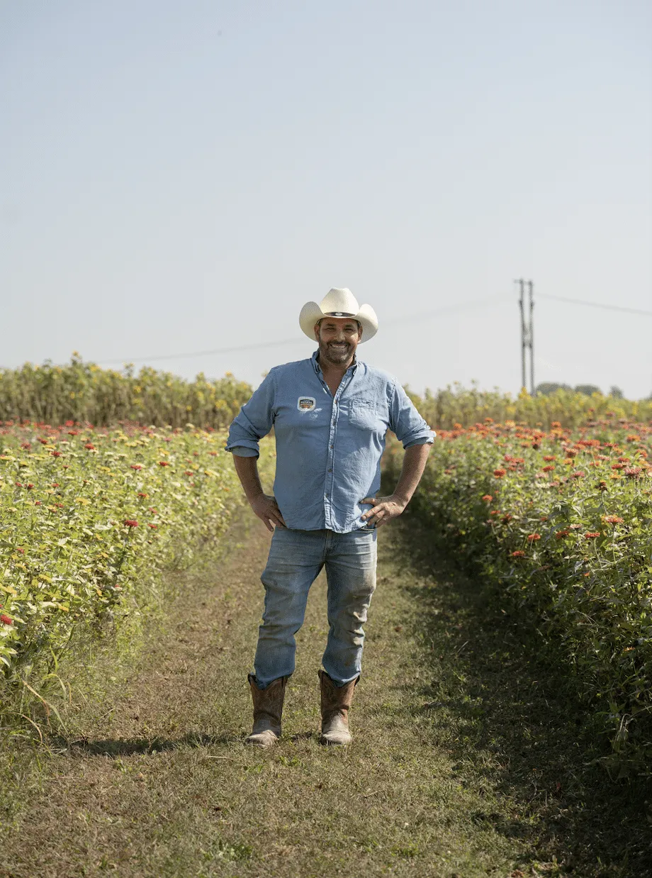 Producteur du Potager Astral souriant dans ses rangées de fleurs
